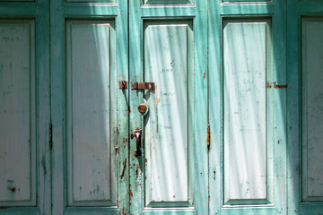 The teal door is made of wood and has three panels. There is a rusty lock on the door.