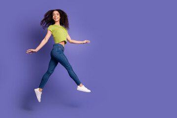 Full size photo of pretty teen girl jump running wear trendy green outfit isolated on purple color background