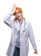 Young redhead woman wearing doctor uniform surprised with hand on head for mistake, remember error. Forgot, bad memory concept.