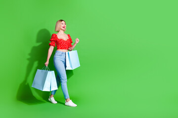 Photo of positive smiling girl go profile side hold shopping bags isolated green color background