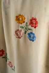 close-up image of white fabric with intricate embroidery featuring colorful flowers and leaves.