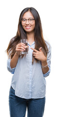 Young asian woman drinking a glass of water over isolated background very happy pointing with hand and finger