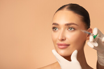 Cosmetologist doctor making filler injection for eyes area to woman, lady getting anti-wrinkle treatment, beige background with free space