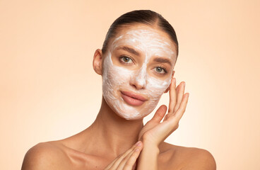 Beautiful young European woman applying facial mask on her face, enjoying skin care and treatment...