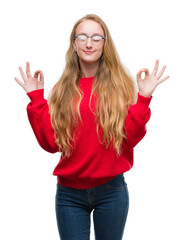 Blonde teenager woman wearing red sweater relax and smiling with eyes closed doing meditation gesture with fingers. Yoga concept.