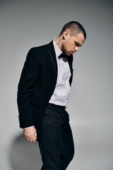 Man in tuxedo against grey backdrop, exuding quiet confidence.