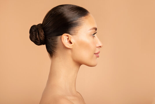 Beauty profile shot of European lady with healthy glowing skin natural makeup, posing isolated on beige background, side view