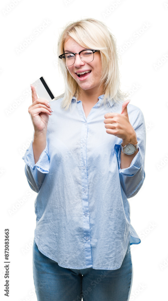 Sticker Young beautiful blonde business woman holding credit card over isolated background happy with big smile doing ok sign, thumb up with fingers, excellent sign