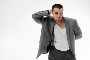 A stylish man in a grey blazer and white t-shirt poses against a white background.