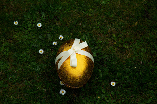 Golden Easter egg with tied up ribbon on grass