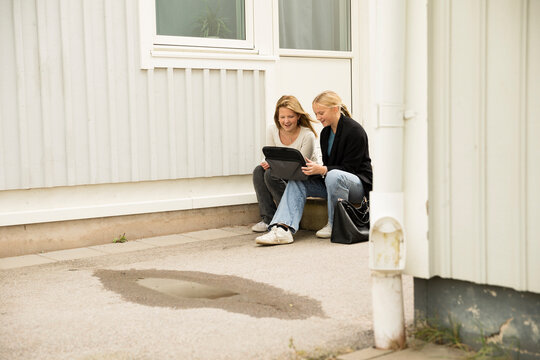 Happy girls using laptop at door step in school building