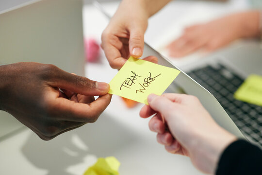 Cropped hands of corporate coworkers holding adhesive note with text teamwork during business meeting