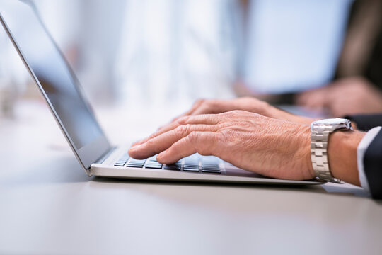 Cropped image of senior businessman using laptop at table in office