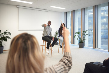 Businessman pointing at colleague to ask question during meeting in office