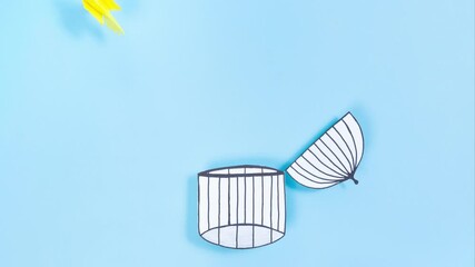 Concept of gaining freedom, removing limiting attitudes, beliefs, liberation from the cage. Yellow bird flies out of the opening cage. Blue background. Flat lay. Stop motion animation.