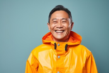 Portrait of a cheerful asian man in his 50s wearing a vibrant raincoat in front of pastel blue background