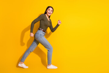 Full body photo of attractive teen woman running fast dressed stylish khaki clothes isolated on yellow color background