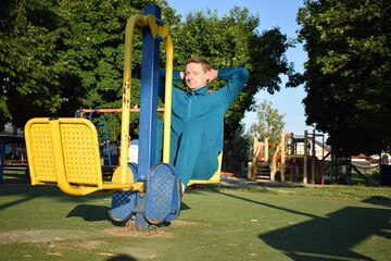 A young man in athletic wear performs morning workout routine at an outdoor gym. He trains...