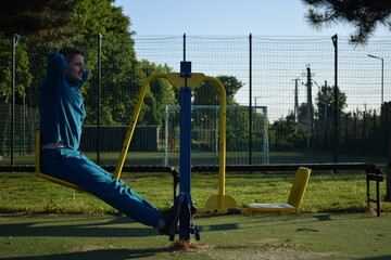 A young man in athletic wear performs morning workout routine at an outdoor gym. He trains...