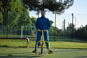 A young man in athletic wear performs morning workout routine at an outdoor gym. He trains...