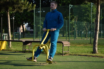 A young man in athletic wear performs morning workout routine at an outdoor gym. He trains...
