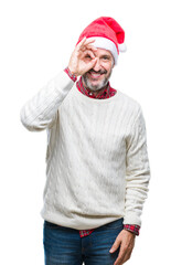 Middle age hoary senior man wearing christmas hat over isolated background doing ok gesture with hand smiling, eye looking through fingers with happy face.