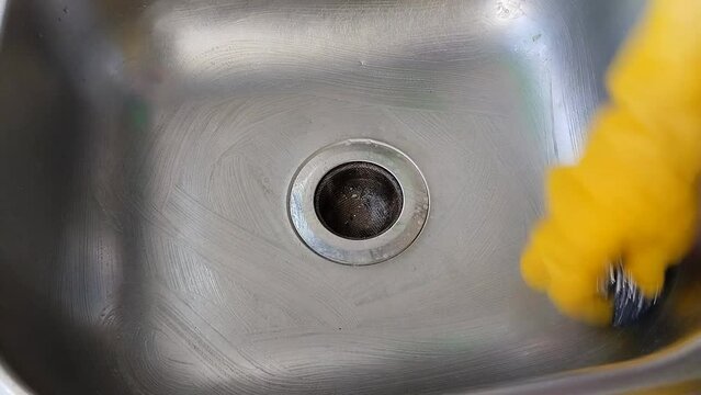 Un primer plano de una mano de mujer con un guante amarillo lavando con una esponja un fregadero