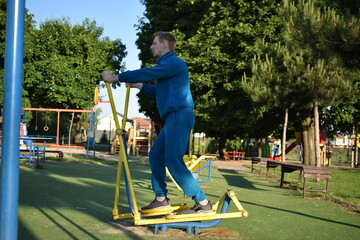 A young man in athletic wear performs morning workout routine at an outdoor gym. He trains...