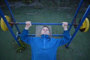 A young man in athletic wear performs morning workout routine at an outdoor gym. He trains...