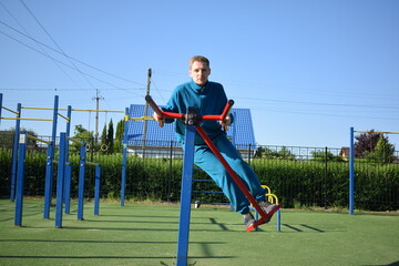A young man in athletic wear performs morning workout routine at an outdoor gym. He trains...