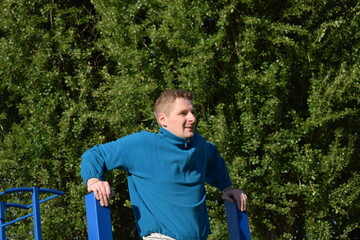A young man in athletic wear performs morning workout routine at an outdoor gym. He trains...