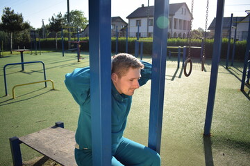 A young man in athletic wear performs morning workout routine at an outdoor gym. He trains...