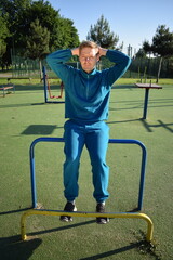 A young man in athletic wear performs morning workout routine at an outdoor gym. He trains...