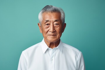 Fototapeta premium Portrait of a tender asian elderly man in his 90s wearing a classic white shirt in front of pastel teal background