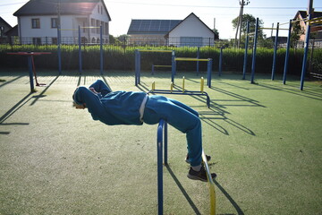 A young man in athletic wear performs morning workout routine at an outdoor gym. He trains...