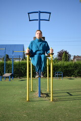 A young man in athletic wear performs morning workout routine at an outdoor gym. He trains diligently on various fitness equipment, building strength endurance, to prepare his body at the sport area