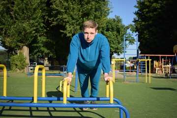 A young man in athletic wear performs morning workout routine at an outdoor gym. He trains...