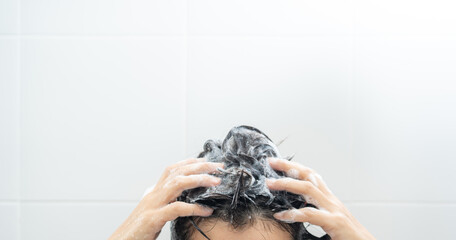 Young woman washing her hair with shampoo foaming. Female rubbing hair and scalp and taking a shower with foam on her head holds fingers in hair in bathroom. Hands to massage head while washing hair.