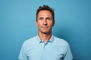 Fototapeta premium Portrait of a satisfied man in his 40s wearing a sporty polo shirt while standing against soft blue background