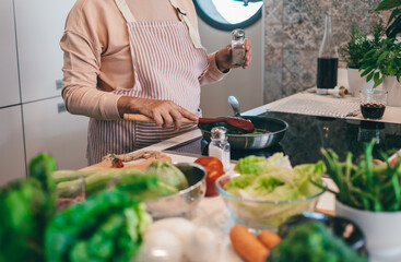 Close up on woman hands  preparing dinner in the kitchen. One elderly female alone cooking. Real lifestyle person testing taste and cook preparation.