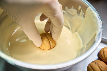 Confectioner coating sweet pastry nuts with melted white chocolate