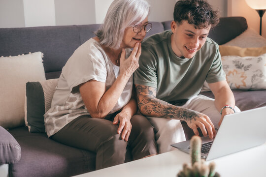 Smiling handsome boy, young nephew teaching technology to his old grandmother using laptop. Senior woman learns to use computer, shopping online, make reservations