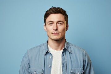 Portrait of a tender man in his 20s sporting a versatile denim shirt in soft blue background