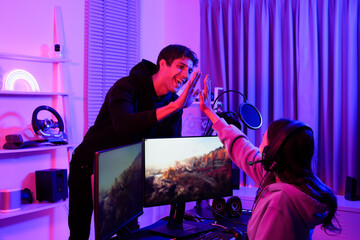 Duo young gamers in a purple neon led light room high five each other after a successful game as a winner surrounded by gaming equipment and teamwork