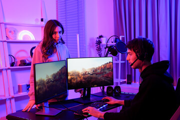 Two young gamers of Asian girlfriend and Caucasian boyfriend in a neon light room engaged in online gaming and streaming with dual monitors and headsets