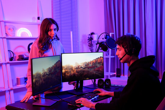 Two young gamers of Asian girlfriend and Caucasian boyfriend in a neon light room engaged in online gaming and streaming with dual monitors and headsets