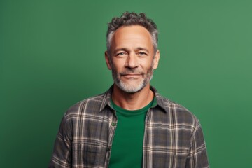 Fototapeta premium Portrait of a smiling man in his 50s wearing a comfy flannel shirt while standing against soft green background