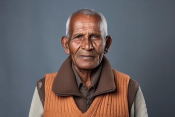 Fototapeta premium Portrait of a satisfied indian man in his 70s dressed in a thermal insulation vest while standing against soft gray background