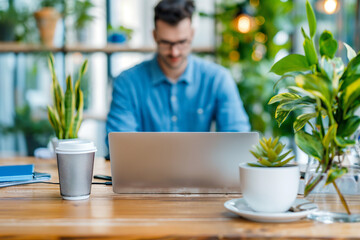 Fototapeta premium A man is sitting at a desk with a laptop and a cup of coffee