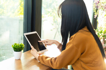 Young Asian woman using a digital tablet while sitting by a window in a cafe. © Kung37